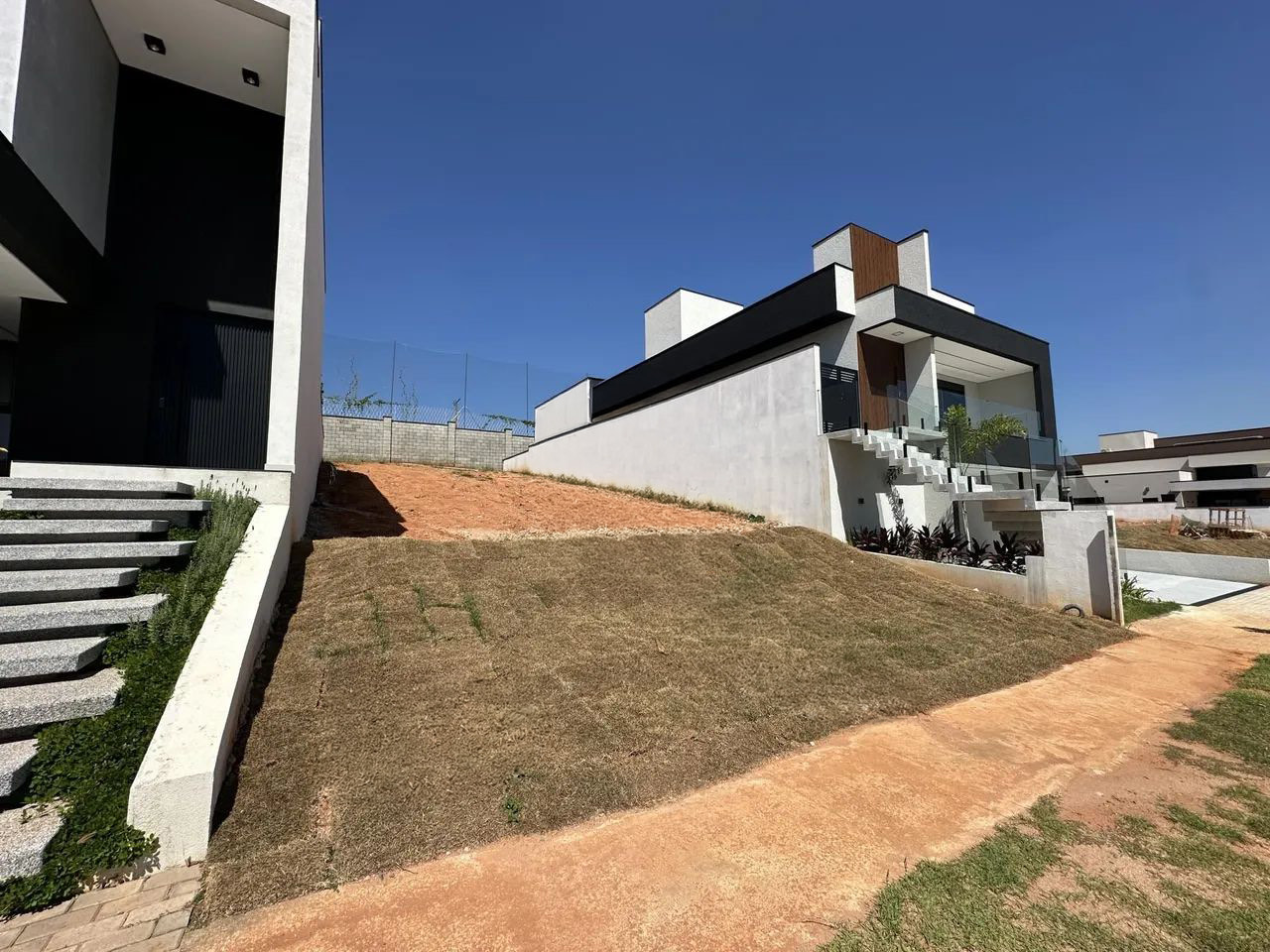 Terreno em aclive com grama seca entre duas casas